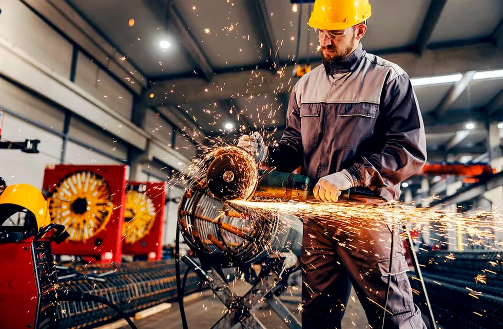 Un trabajador de la industria metalúrgica procesando una pieza metálica con una amoladora.
