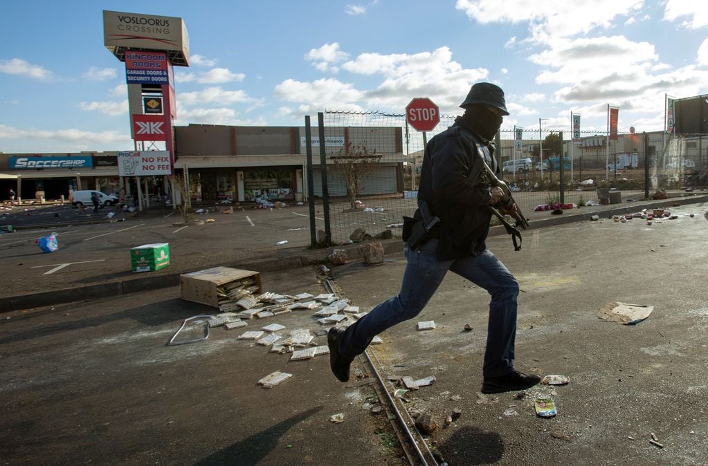 Un oficial de metro vestido de civil, persigue saqueadores saqueadores en un centro comercial en Soweto, Johannesburgo.