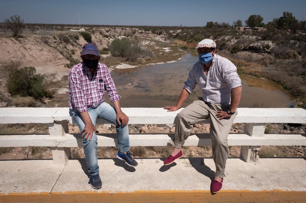 Dos productores esperan sentados sobre el puente del río Desaguadero.