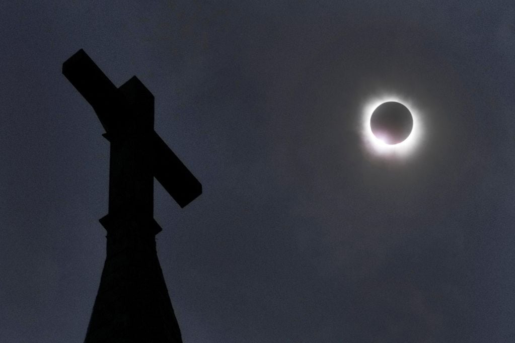 La luna cubre parcialmente el sol durante un eclipse solar total, como se ve sobre una cruz en lo alto del campanario de la Iglesia Evangélica Luterana de Nueva Suecia el lunes 8 de abril de 2024 en Manor, Texas. (Foto AP/Charles Rex Arbogast)