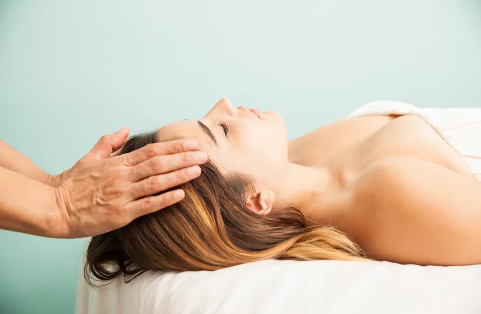 Profile view of a cute young woman getting her energy balanced at a reiki session in a health clinic and spa