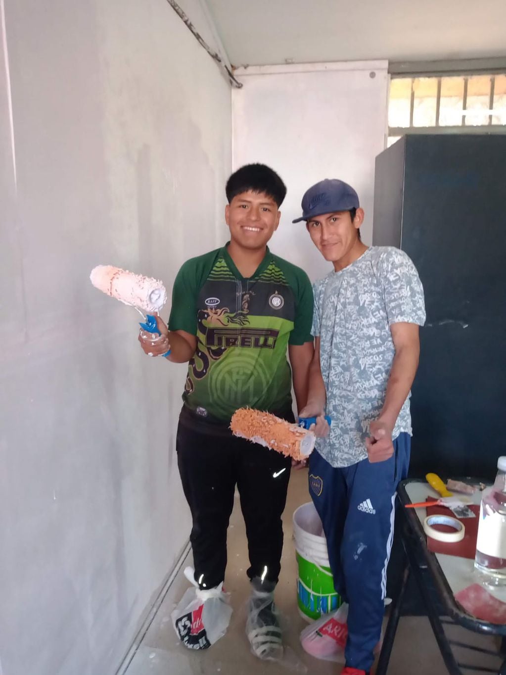 Dos alumnos posan para la foto mientras pintan su escuela.