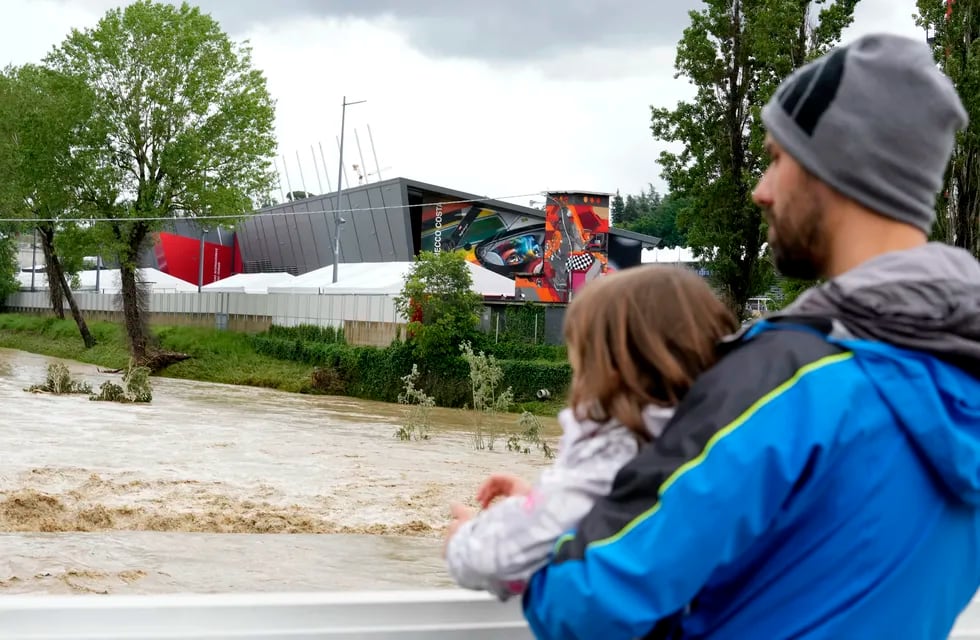 Un hombre con un niño en brazos contempla la crecida del río Santerno, y en el fondo de ve el circuito Enzo e Dino Ferrari en Imola, Italia, 17 de mayo de 2023. Las inundaciones obligaron a cancelar el GP Fórmula 1 de la Emilia Romagna. / AP