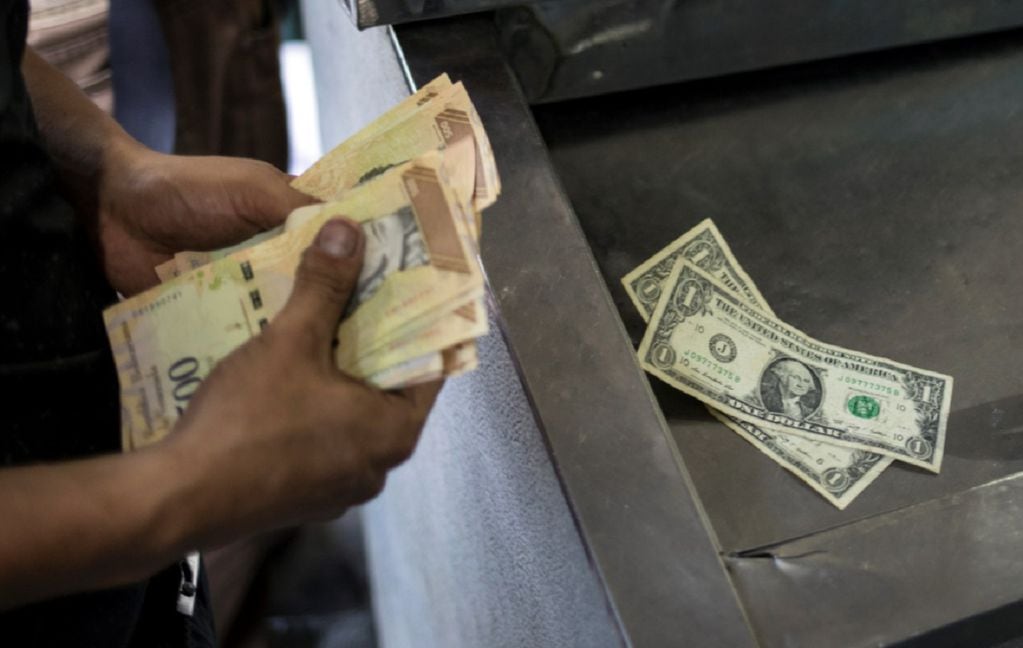 Un hombre cuenta sus bolívares y dólares para pagar artículos en un mercado en Caracas, Venezuela (AP)