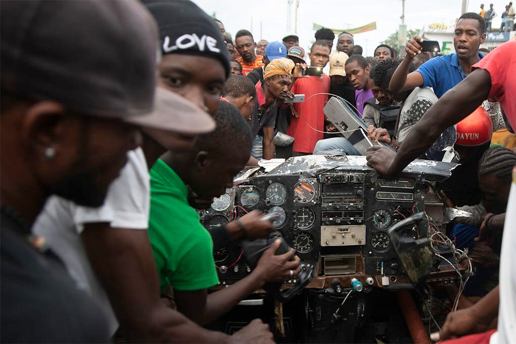 Residentes observan la cabina de un avión Cessna 207 que se estrelló en la comunidad de Carrefour, en Puerto Príncipe, Haití, el 20 de abril de 2022. El pequeño aeroplano se estrelló cuando trataba de aterrizar e impactó contra un camión que transportaba botellas de soda. En el accidente fallecieron al menos cinco personas y varias más resultaron heridas, según las autoridades. (AP Foto/Odelyn Joseph)