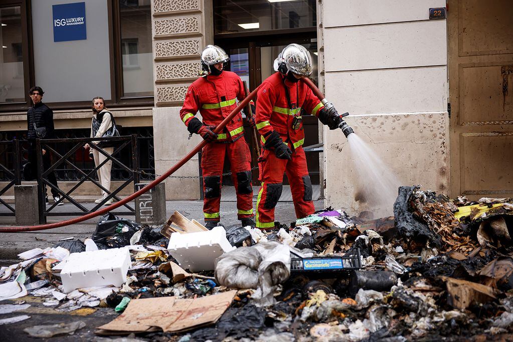 Protestas en Francia. Bomberos controlando los restos de un incendio de basura de las protestas de anoche contra el proyecto de ley de jubilación en París. (AP)