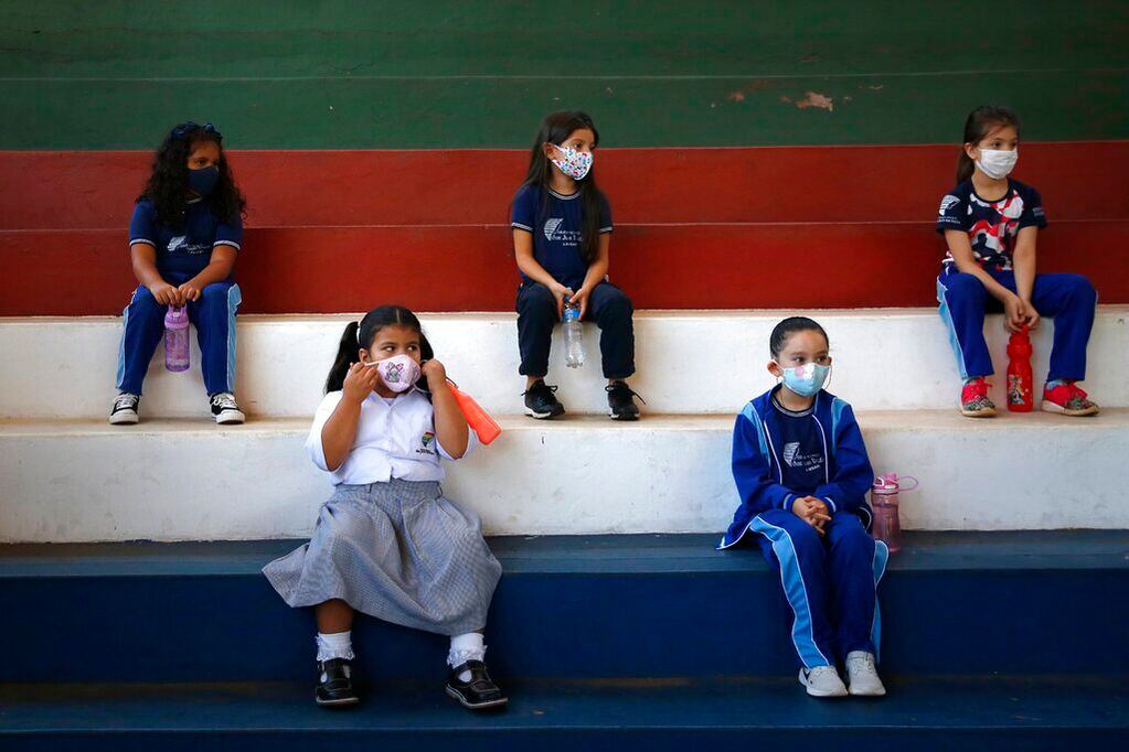 Estudiantes de primer grado, con mascarilla para protegerse del coronavirus, se sientan manteniendo la distancia social en un gimnasio durante una clase en la escuela técnica San Juan Bautista, en Lambare, Paraguay