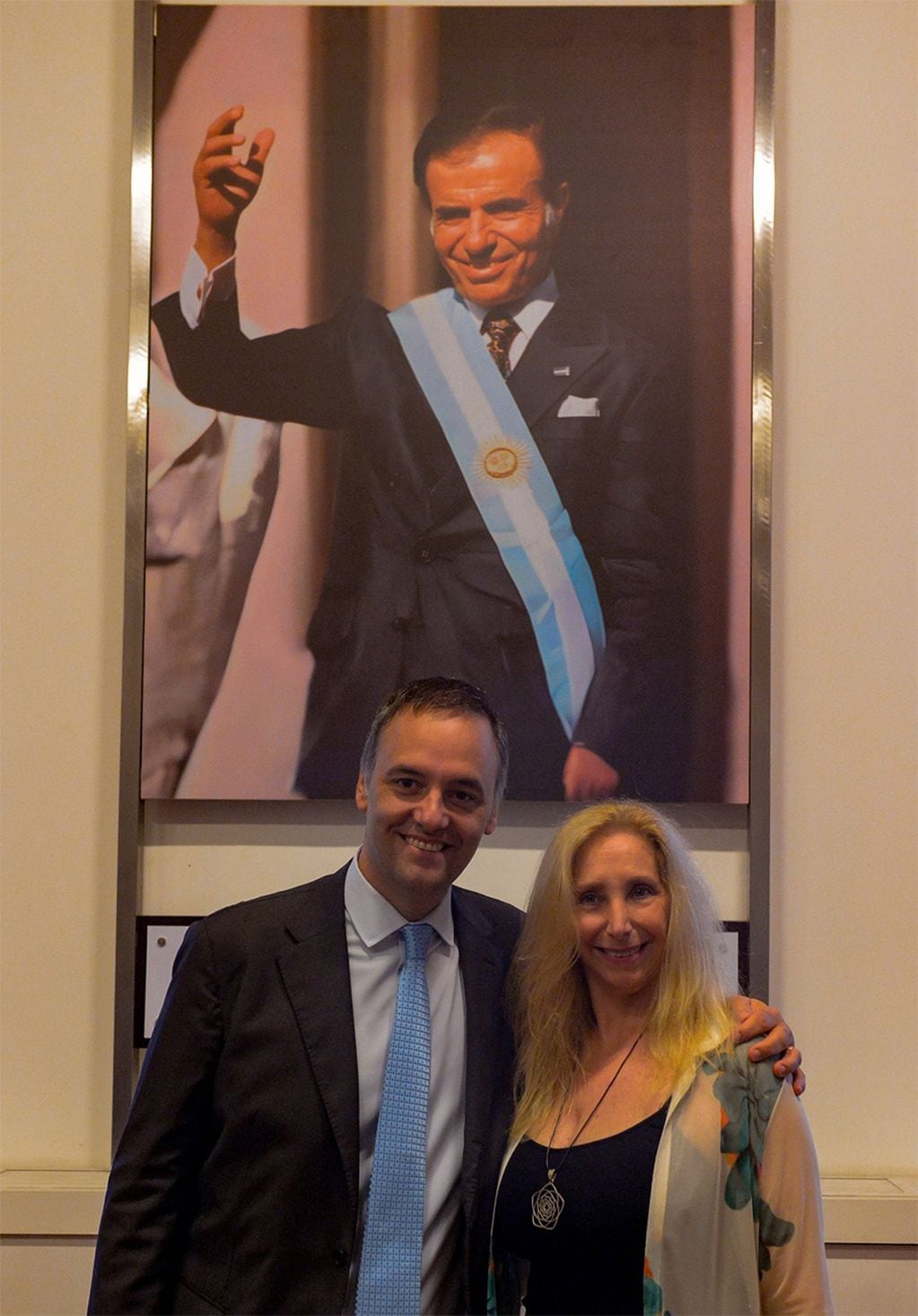 El vocero presidencial Manuel Adorni y la secretaria general de la presidencia Karina Milel posan mostrando el cuadro de Carlos Saúl Menem en el Salón de los Próceres de Casa Rosada (Manuel Adorni/X).