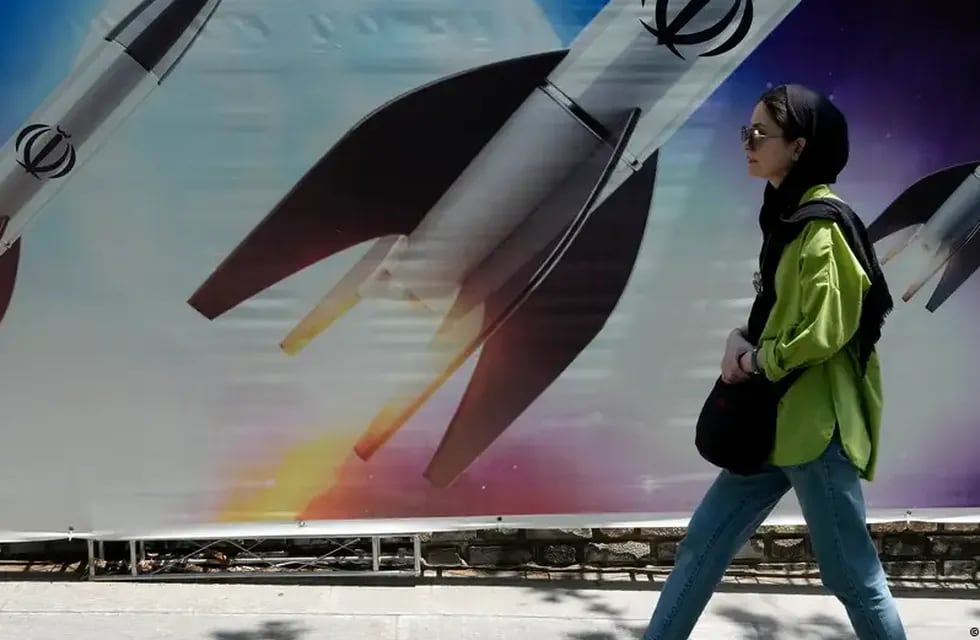 Una mujer camina junto a una pancarta que muestra el lanzamiento de misiles, en el norte de Teherán el viernes 19 de abril de 2024. En los misiles, la palabra con la que son "decorados" reza: "Alá" (Dios).