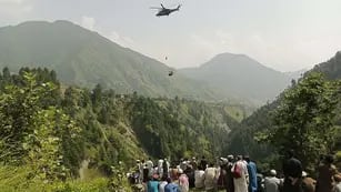 Varias personas observan cómo un soldado del Ejército desciende de un helicóptero durante la misión de rescate. (AFP/Télam)