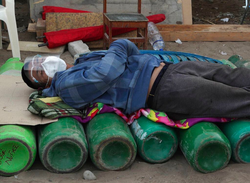 Un hombre duerme sobre bombonas de oxígeno mientras espera a que abra un comercio para rellenar la suya, en el vecindario Villa El Salvador de Lima, Perú