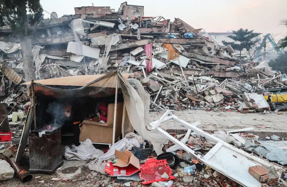 Personas se protegen en una tienda de campaña cerca de un edificio derrumbado tras un fuerte terremoto en Hatay, Turquía (EFE)