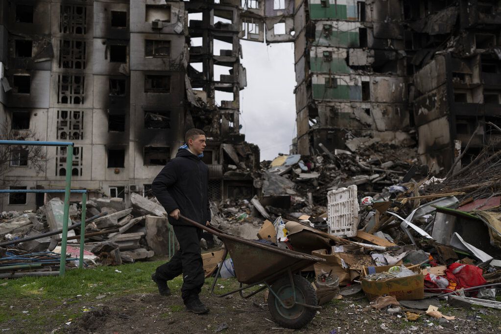 Un joven empuja una carretilla frente a un edificio residencial destruido, el domingo 10 de abril de 2022. 