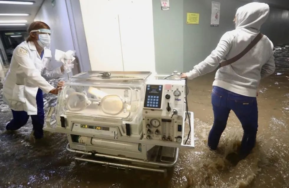Enfermeras y médicas trasladan incubadoras para que las leven a un hospital seguro, ya que las inundaciones han afectado el servicio eléctrico.