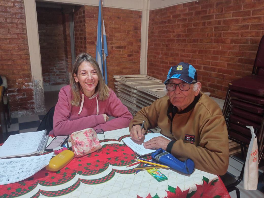 Jorge aprende a leer y escribir en uno de los talleres junto a su docente Carmen García. Cuando tenga teléfono, aprenderá a utilizarlo. Tiene 77 años. | Foto: gentileza