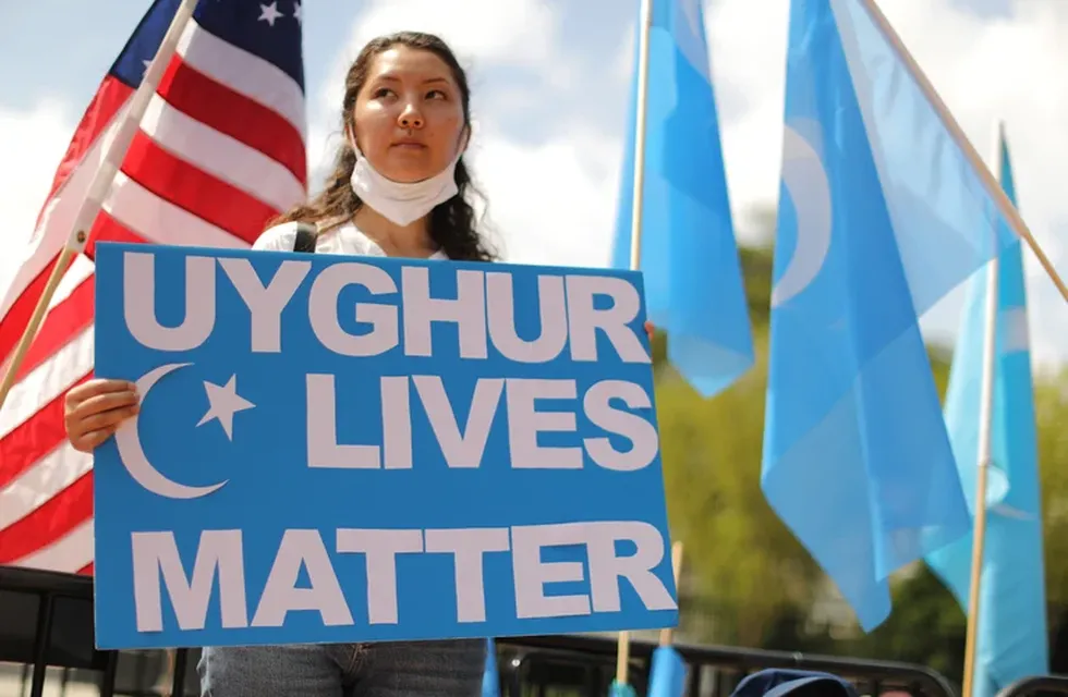 Una mujer sostiene una pancarta en la que se lee "Las vidas de los uigur importan" durante una protesta en EE.UU.

De fondo, la bandera estadounidense y la bandera de la minoría uigur.