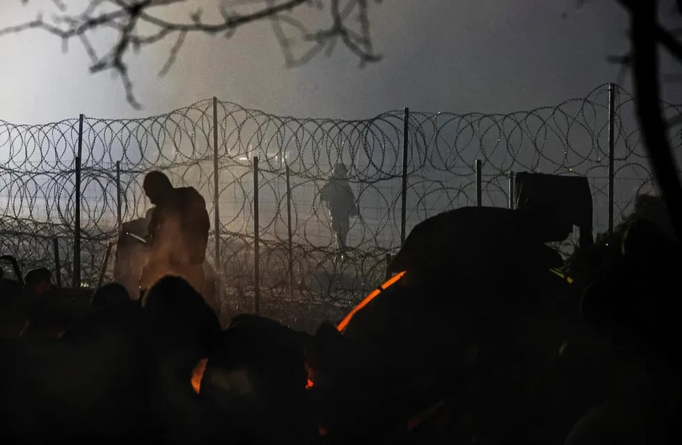 Un guardia fronterizo polaco patrulla cerca de una cerca de alambre de púas mientras los migrantes se calientan cerca de la fogata en la frontera entre Bielorrusia y Polonia cerca de Grodno. (AP)