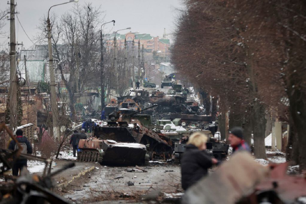 La gente mira los restos destripados de vehículos militares rusos en una carretera en la ciudad de Bucha, cerca de la capital, Kiev, Ucrania (AP)