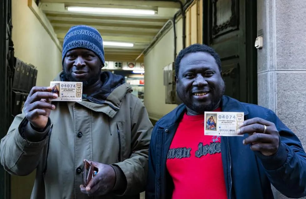Ibrahim y otro hombre, oriundos de Gambia y residentes de Olot, posan frente la administración de lotería número 1 de Olot (Girona) con su billete ganador.
