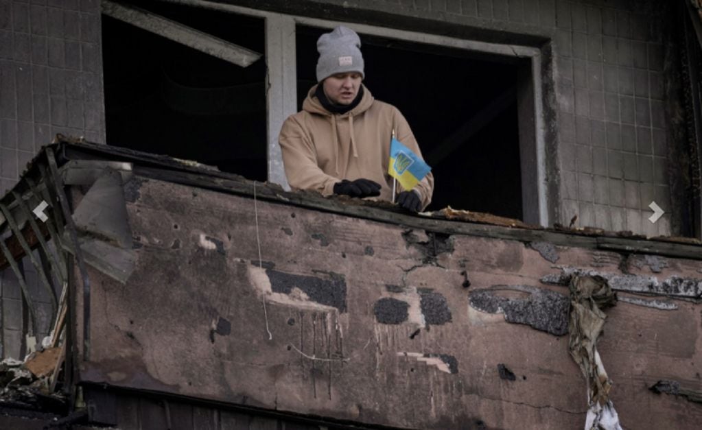 Un hombre coloca una pequeña bandera ucraniana en el balcón quemado de un apartamento en un bloque que fue destruido por un ataque de artillería en Kiev, Ucrania, el lunes 14 de marzo de 2022. (AP)