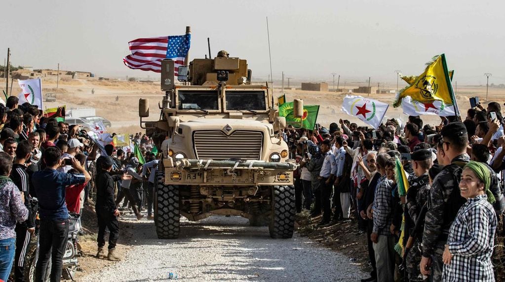 Un tanque estadounidense pasa entre civiles y guerrilleros afines al PKK y al YPG al norte de Siria en 2019, cuando el expresidente de EE.UU. Donald Trump ordenó la retirada de las tropas de esa región. Joe Biden restabeció la presencia apenas asumió su gobierno.