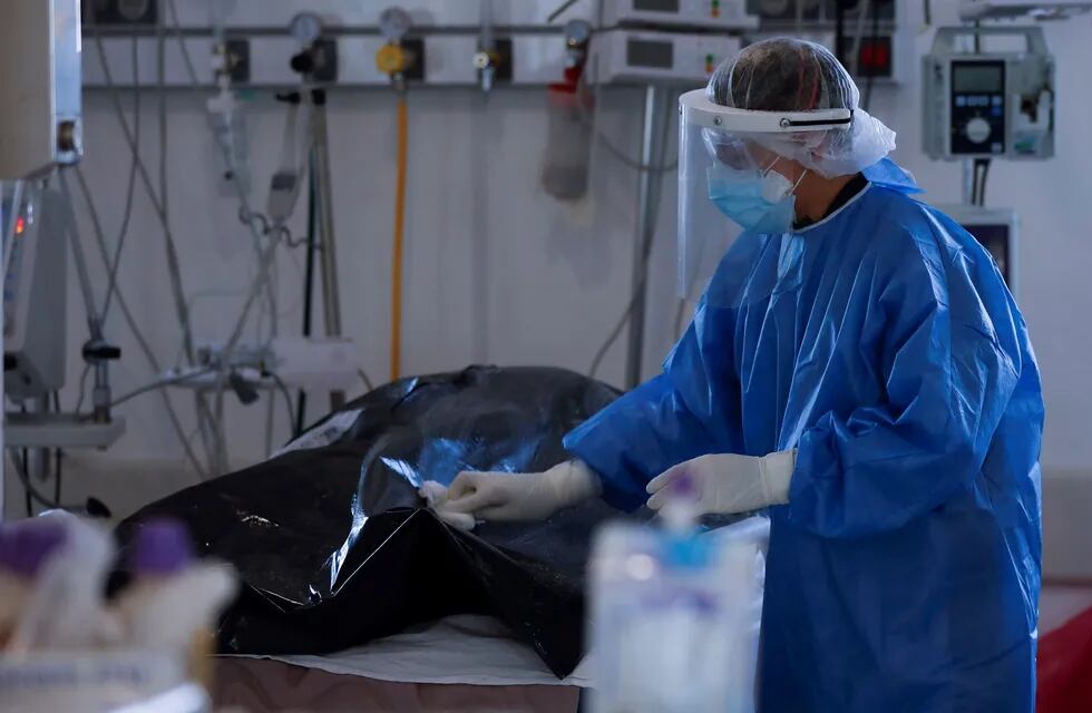 Un trabajador de salud limpia la bolsa para cadáveres de una víctima de COVID-19 en la unidad de cuidados intensivos (UCI) en un hospital bonaerense.
