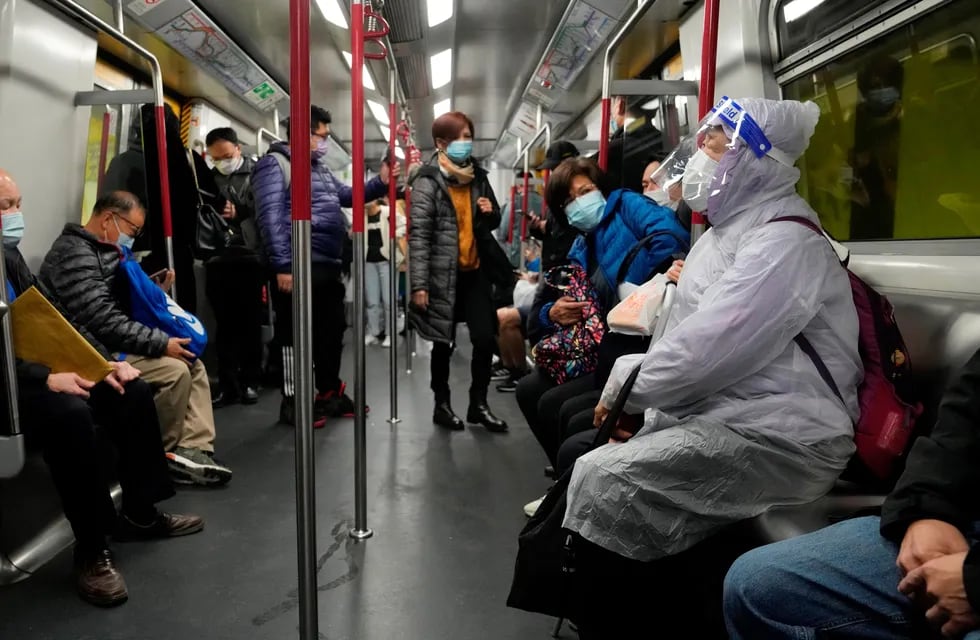 Una mujer con mascarilla y ropa protectora en el subte de Hong Kong.