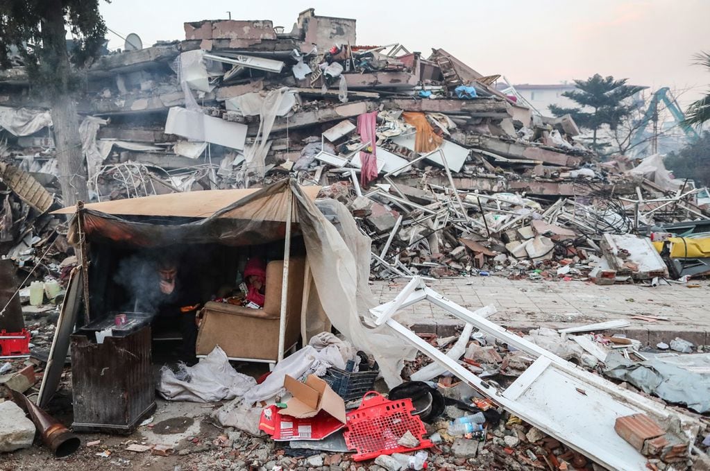 Personas se refugian en una tienda de campaña cerca de un edificio derrumbado tras un fuerte terremoto en Hatay, Turquía (EFE)