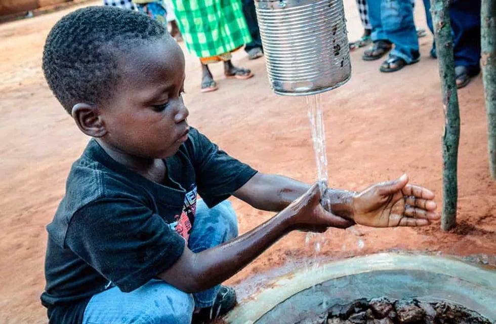 Un niño se lava las manos con agua que brota de una lata, luego de hacer fila para poder acceder a ella. El agua potable es un bien muy escaso.