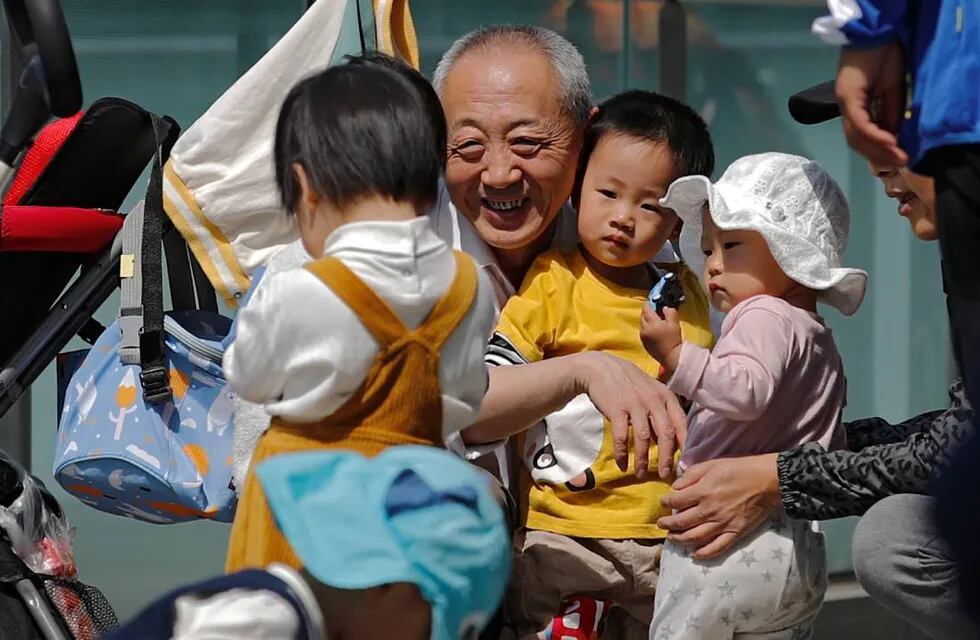 Un anciano juega con niños cerca de un edificio de oficinas comerciales en Pekín - Foto de Andy Wong/AP