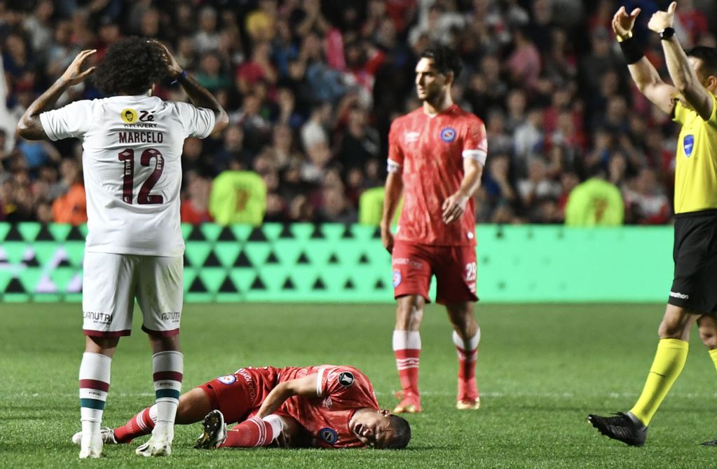 El defensor de Argentinos Juniors Luciano Sánchez y la dura lesión en la rodilla, y el lamento de Marcelo, el experimentado jugador de Fluminense. (Fotobaires)