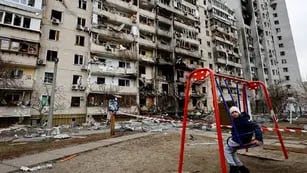 Un nene se sienta en un columpio frente a un edificio residencial dañado en Kiev, Ucrania, este viernes 25 de febrero de 2022