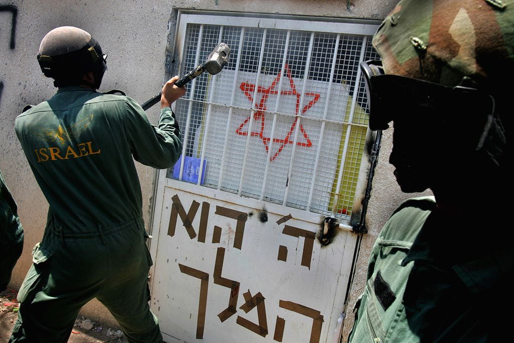 Israeli troops use a hammer as they try to gain access into a Yeshiva,  religious school, during the forced evacuation of the northern West Bank Jewish settlement of Homesh Tuesday Aug. 23, 2005. Thousands of troops pushed into two northern West Bank settlements, Homesh and Sanur, Tuesday and began clearing out hundreds of extremists holed up inside, in the last phase of Israel's dismantling of 21 settlements in the Gaza Strip and four in the West Bank. Writing on the door under a Star of David reads in Hebrew "God is the King" (AP Photo/Oded Balilty)  MIDEAST ISRAEL PALESTINIANS SETTLEMENTS HOMESH  PSE 1484911