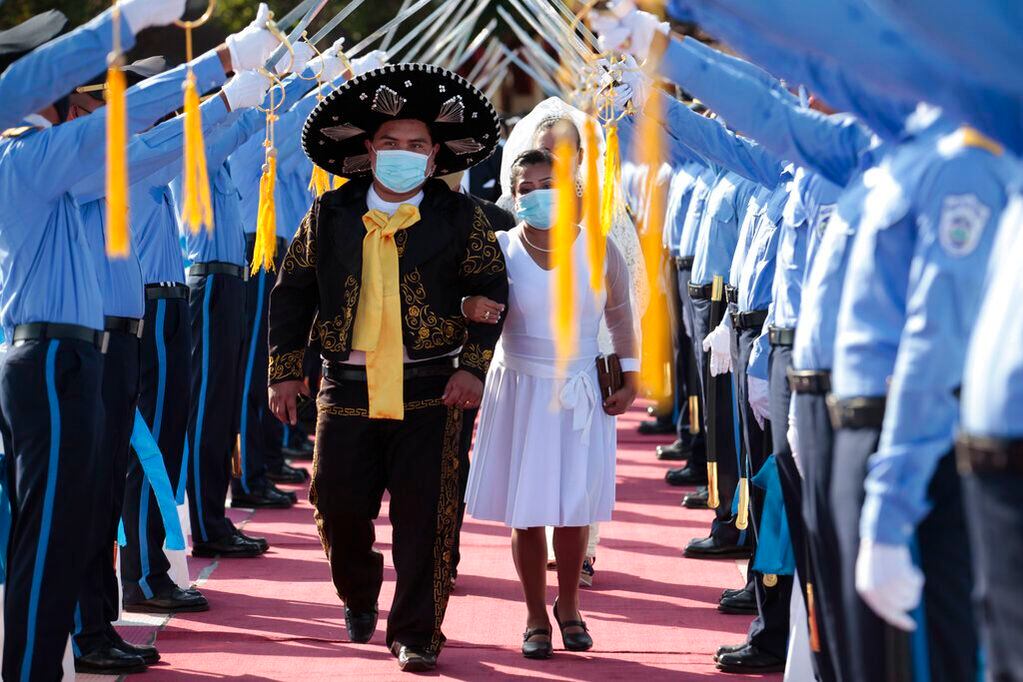 Una pareja de recién casados, con mascarilla por la pandemia del coronavirus, caminan por debajo de un arco de espadas durante la 18va edición de una misa de boda multitudinaria organiza por una emisora de radio local, en Managua, Nicaragua