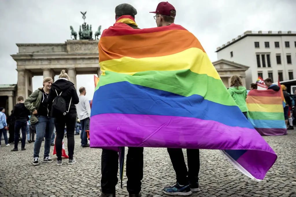 Dos personas identificadas con la nueva unión homosexual festejan en Berlín cubiertos con una bandera arcoiris.