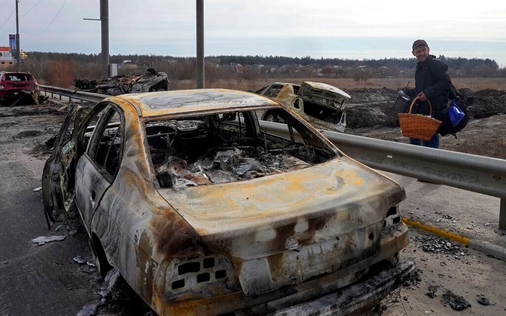 Un habitante pasa al lado de autos incendiados tras un ataque ruso mientras abandona Irpin, su pueblo natal. Foto: AP / Efrem Lukatsky