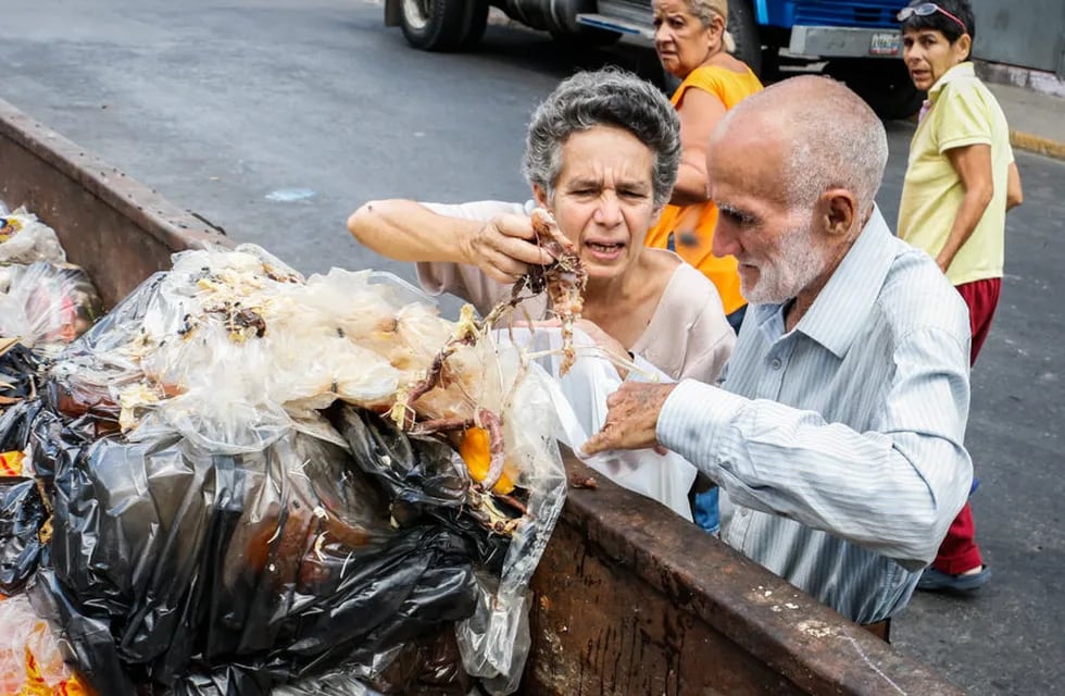 Dos adultos mayores revuelven basura en busca de comida en Venezuela.